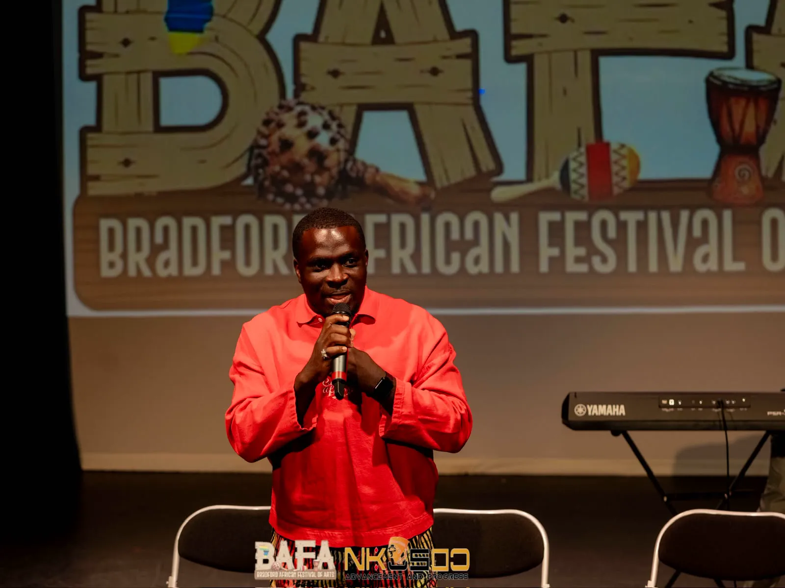 MC Crown performing with a microphone in front of the Bradford African Festival of Arts backdrop