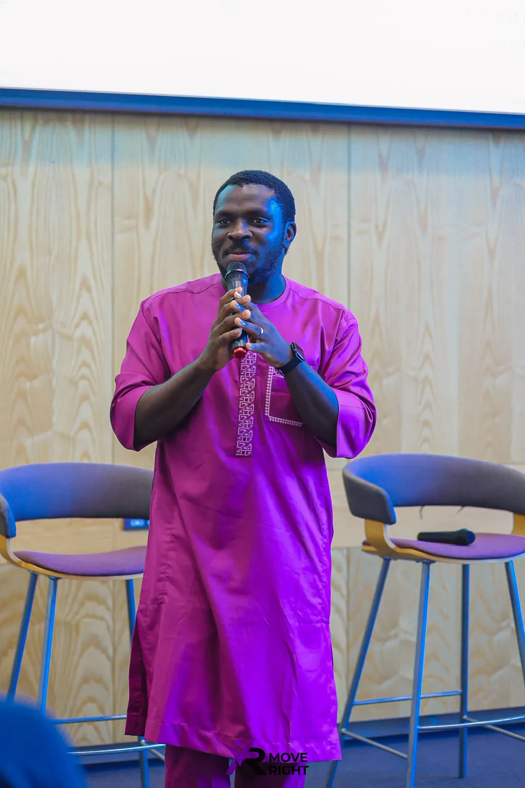 MC Crown in a purple outfit speaking into a microphone before an audience