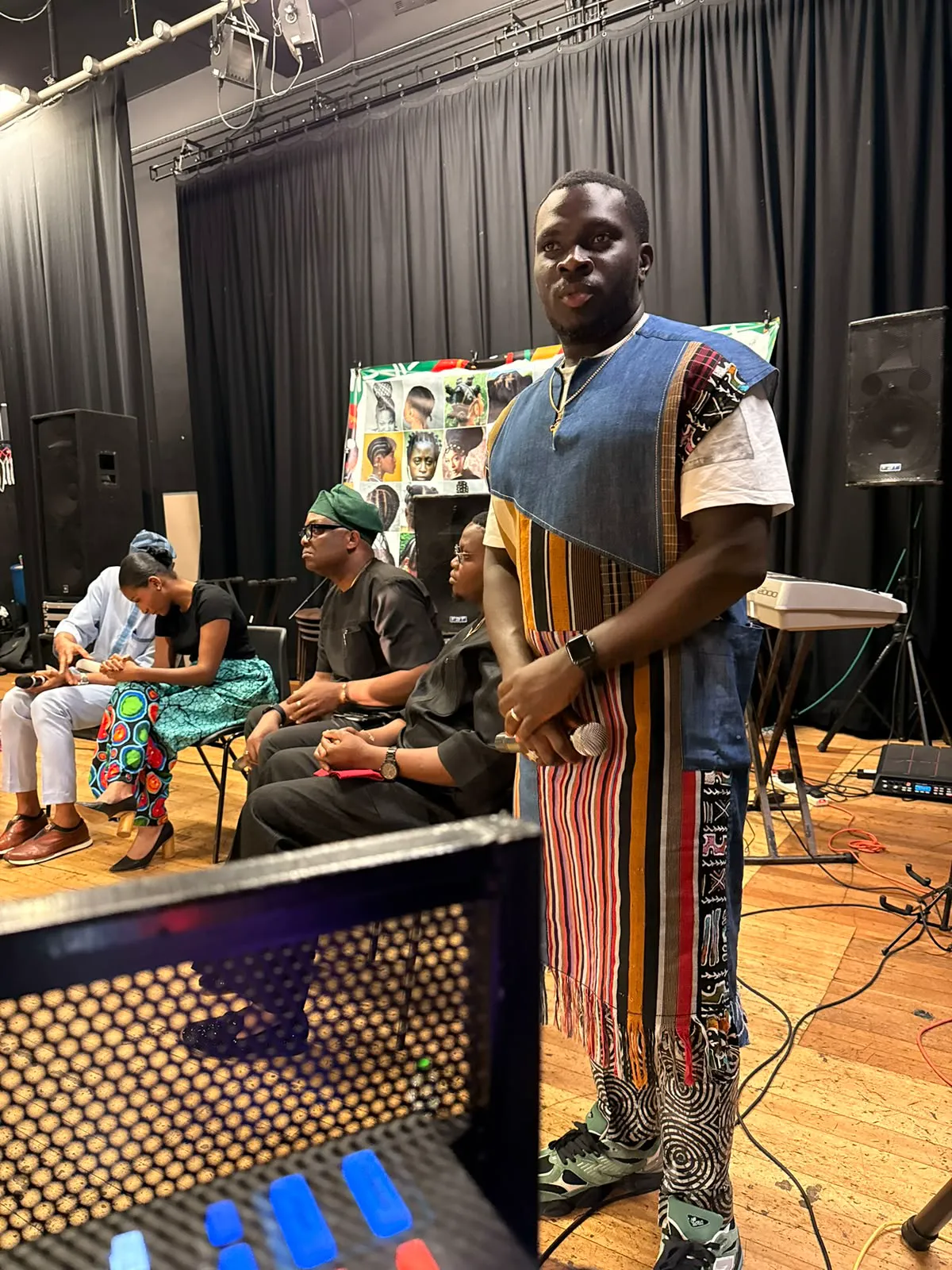 MC Crown holding a microphone in a striped cultural costume on stage